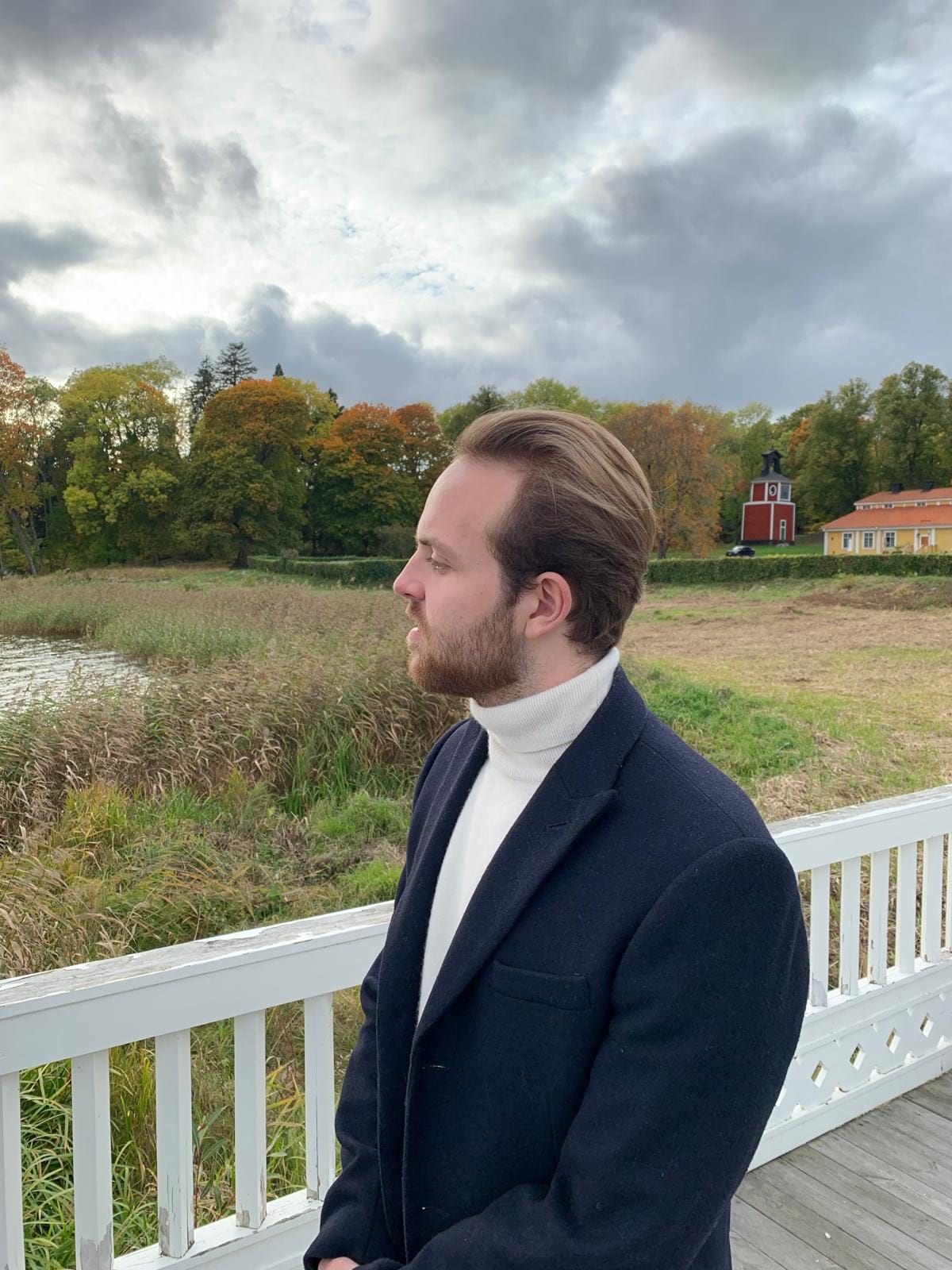 Melker Pasternak Ivarsson in an overcoat and turtleneck on a jetty, autumn in the Swedish countryside